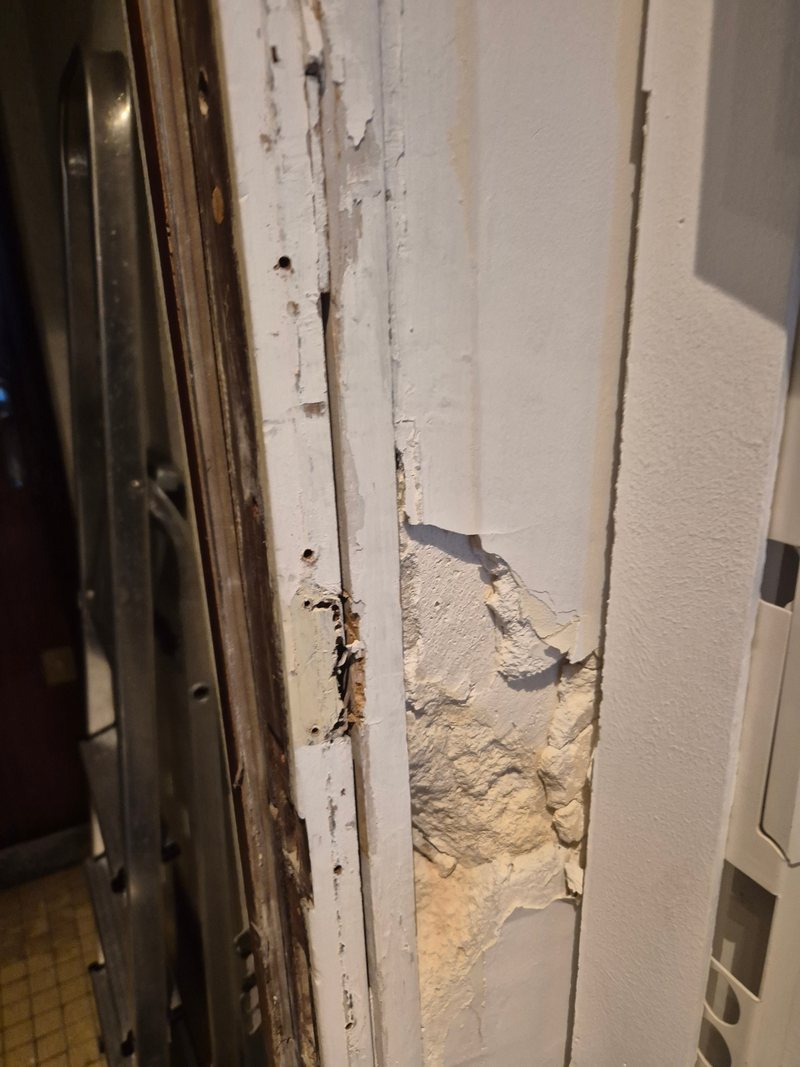 Bâti de porte endommagé et enduit éclaté après une effraction